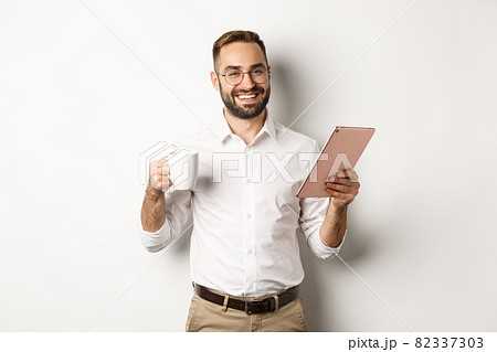 Satisfied boss drinking tea and using digital tablet, reading or working, standing over white background Satisfied boss drinking tea and using digital tablet, reading or working, standing over white background 82337303