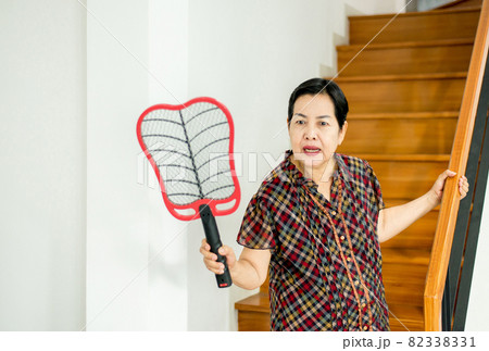 Elderly woman using mosquito swatter at home,Female with mosquito electric net racket 82338331