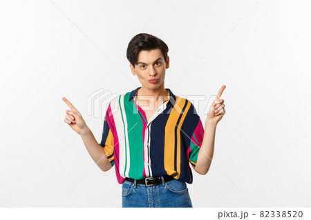Handsome gay man pointing fingers sideways, showing two variants, demonstrate promos, standing over white background Handsome gay man pointing fingers sideways, showing two variants, demonstrate promos, standing over white background 82338520