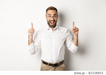 Excited businessman checking out advertisement, pointing and looking up with happy face, standing against white background 82338955
