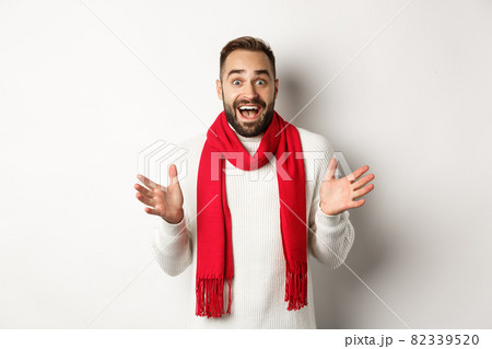 Christmas holidays and celebration concept. Bearded guy looking surprised at new year promo offers, gasping amazed, wearing red scarf and sweater, white background 82339520