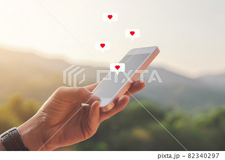 Close up woman hand hold using smart phone with heart icon at top of mountain and sunset sky background. 82340297