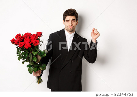 Image of elegant and sassy man in black suit, looking confident and holding bouquet of red roses, going on a romantic date, standing against white background Image of elegant and sassy man in black suit, looking confident and holding bouquet of red roses, going on a romantic date, standing against white background 82344753