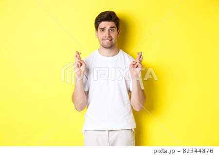 Nervous guy crossing fingers for good luck, hoping for something, standing over yellow background Nervous guy crossing fingers for good luck, hoping for something, standing over yellow background 82344876