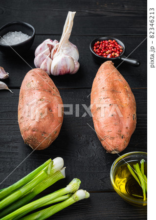 Raw whole sweet potatoe with ingredients, on black wooden background 82346213