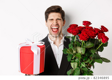 Image of sad guy in suit, got rejected and crying, holding bouquet of roses and present, standing miserable against white background Image of sad guy in suit, got rejected and crying, holding bouquet of roses and present, standing miserable against white background 82346895