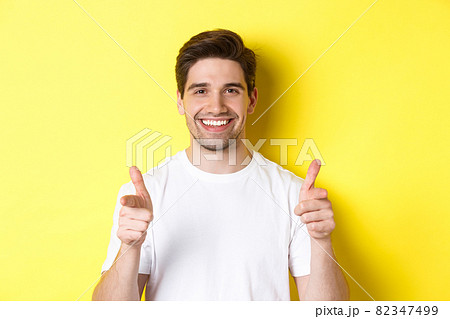 Confident man pointing fingers at camera and smiling, praising you, standing over yellow background 82347499