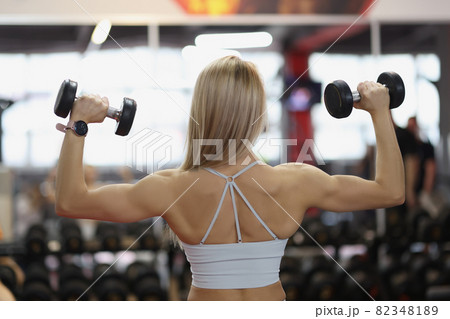Woman lifts dumbbells in gym. Best biceps exercises 82348189