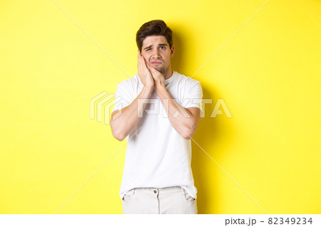 Sad guy complaining on toothache, touching swallen cheek and looking upset, standing over yellow background 82349234