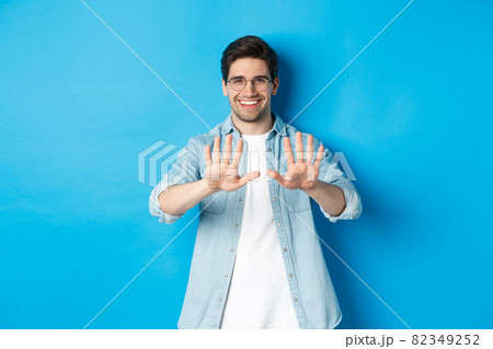 Image of smiling man looking satisfied at his manicure, visit beauty salon, standing over blue background 82349252
