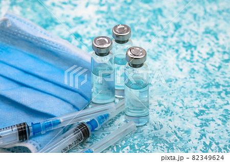 Prevention of seasonal diseases. Vaccination against covid-19. Medical vials, syringes and mask on a green background. 82349624