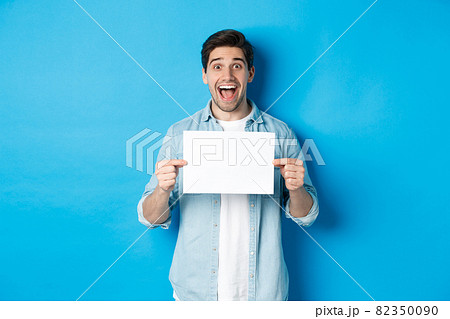 Excited man making fantastic announcement, showing logo or sign on blank piece of paper, standing over blue background Excited man making fantastic announcement, showing logo or sign on blank piece of paper, standing over blue background 82350090