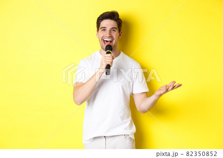 Happy man entertainer performing, talking in microphone, making speech or stand-up show, standing over yellow background 82350852