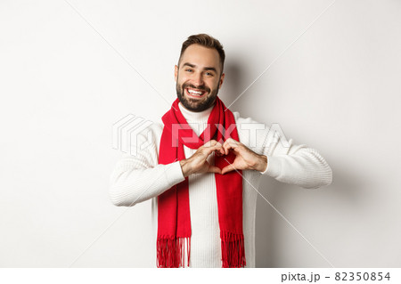 Christmas holidays and New Year concept. Happy father showing heart sign and smiling, I love you gesture, wearing winter sweater and scarf, white background 82350854