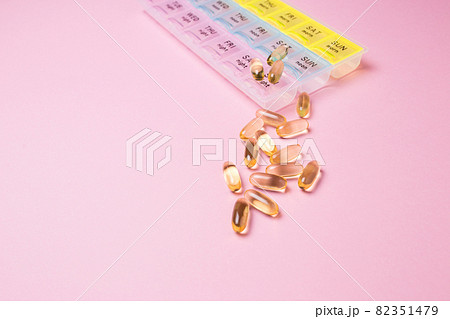 Organizer for medical pills on a pink isolated background close-up. Organization of taking pills of the day. Transparent vitamins lie nearby. 82351479