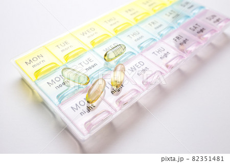 Organizer for medical pills on a white isolated background close-up. Organization of taking pills of the day. Transparent vitamins lie nearby 82351481