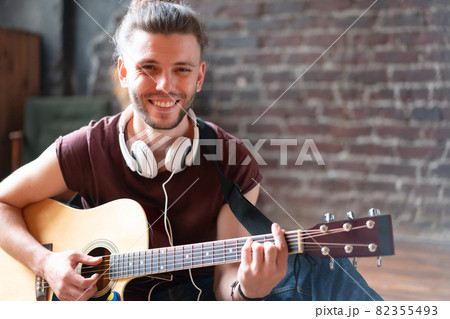 Handsome young man playing acoustic guitar sitting floor living loft room Handsome young man playing acoustic guitar sitting floor living loft room 82355493