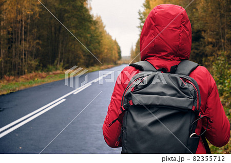 A woman with a Backpack and a Red Jacket Walks Along the Forest Car Road. A woman with a Backpack and a Red Jacket Walks Along the Forest Car Road. 82355712