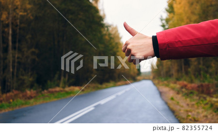 A Woman in a Red Jacket Trying to Stop a Car on the Forest Road. A Woman in a Red Jacket Trying to Stop a Car on the Forest Road. 82355724