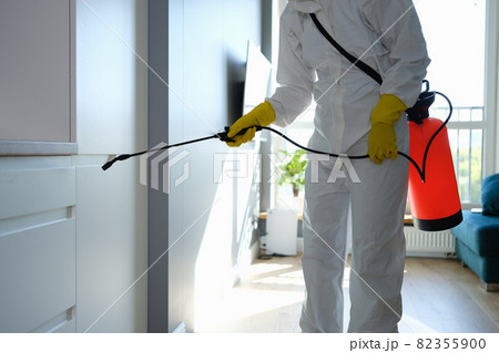 Worker in protective overalls and gloves disinfecting apartment 82355900