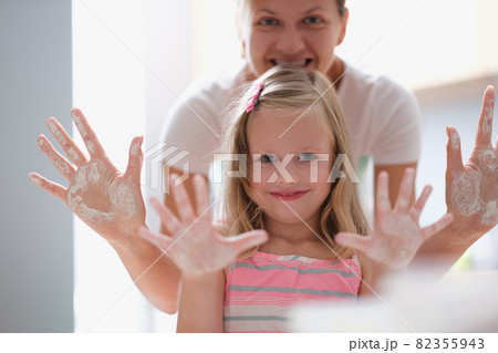 Mom and little girl showing palms of hands in flour Mom and little girl showing palms of hands in flour 82355943