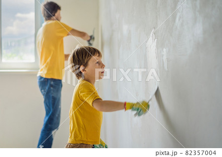 Man with his son makes repairs at home, he teaches children to plaster the walls with a spatula in his hands 82357004