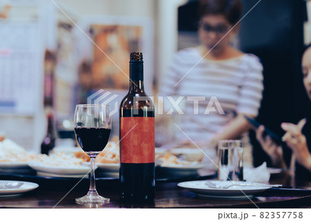 Wine bottle and glasses on dinner table with woman in background. Wine bottle and glasses on dinner table with woman in background. 82357758