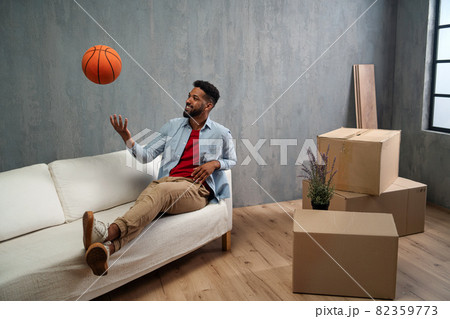 Happy young man with basketball celebrating moving home surrounded by packing boxes, new living concept. 82359773