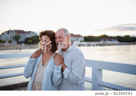 Happy senior couple hugging outdoors on pier by sea, looking at view. 82360591