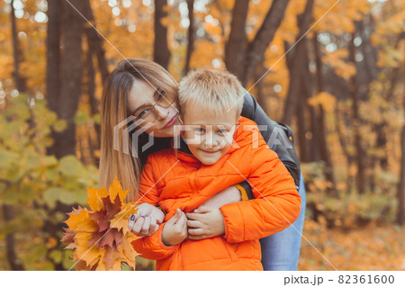 Mother hugging her child during walk in autumn park. Fall season and single parent concept. Mother hugging her child during walk in autumn park. Fall season and single parent concept. 82361600