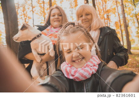 Three generations of women and dog feel fun look at camera posing for self-portrait picture together, funny excited child, mom and grandmother have fun enjoy weekend take selfie on gadget in autumn 82361601
