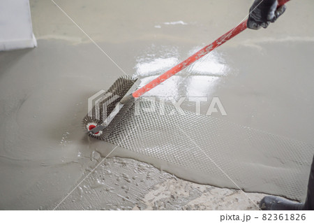 plasterer during floor covering works with self-levelling cement mortar, uses a needle roller plasterer during floor covering works with self-levelling cement mortar, uses a needle roller 82361826