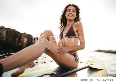 Beautiful young woman sitting on a stand up paddle board in sea Beautiful young woman sitting on a stand up paddle board in sea 82362434