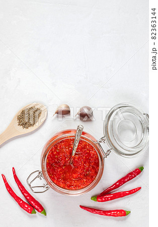 Adjika with a jar on a white background. Hot chili pepper sauce paste harissa. Vertical orientation. Copy space, top view, flat lay. 82363144