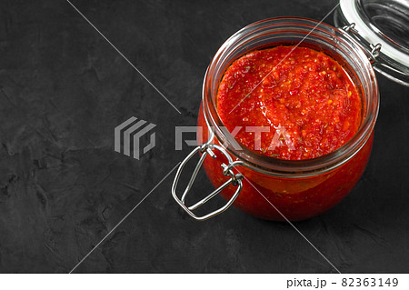 Harissa sauce. Adjika. Hot chili pepper sauce in a jar on a black background closeup. Tunisia, Georgian and Arabic cuisine. Copy space. Harissa sauce. Adjika. Hot chili pepper sauce in a jar on a black background closeup. Tunisia, Georgian and Arabic cuisine. Copy space. 82363149