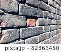 Single red brick lies in niche of old grey brickwall among other bricks and spiderweb. Angled photo of facade of ancient wall with tiled brickwork. Weathered stone texture concept 82366450