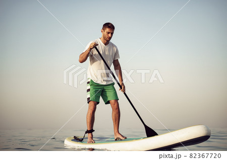 Young man in t-shirt and shorts floating on SUP board Young man in t-shirt and shorts floating on SUP board 82367720