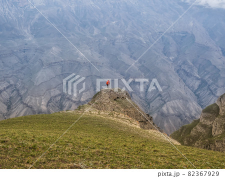Small silhouette of woman with a backpack stands with her back over the cliff. Solitude in the mountains, solo travel concept. 82367929