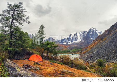 Camping on a autumn high-altitude plateau. Orange tent under the rain. Peace and relaxation in nature. Upper Shavlin Lake in the Altai. 82368555