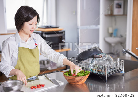 キッチンでサラダを盛り付けるエプロン姿の若い女性 キッチンでサラダを盛り付けるエプロン姿の若い女性 82368728