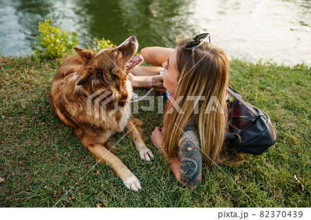 Close up of young female with her dog sitting on grass in park 82370439