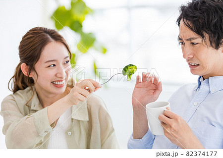 ブロッコリーを食べ飽きている男性と食べさせようとする女性 82374177