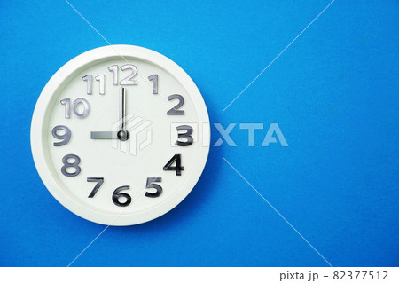White round clock showing Nine o'clock on blue background White round clock showing Nine o'clock on blue background 82377512
