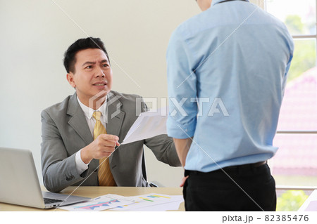 Asian businessman manager in suit holding paperwork and blaming for young employee with anger and serious gesture look like he comments as disagree or unacceptable for his project work 82385476