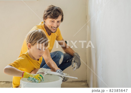 Man with his son makes repairs at home, he teaches children to plaster the walls with a spatula in his hands 82385647