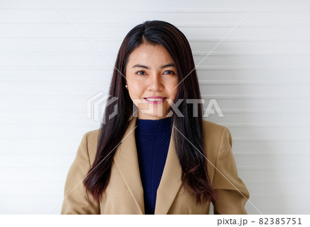 Horizontal close-up portrait shot of an attractive smiling young adult Asian woman in the formal brown suit and blue clothes looking at the camera isolated with white background in the studio Horizontal close-up portrait shot of an attractive smiling young adult Asian woman in the formal brown suit and blue clothes looking at the camera isolated with white background in the studio 82385751