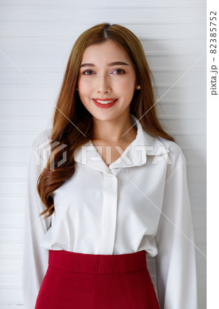 Horizontal half-body portrait shot of a confident Asian woman in a simple modern long sleeve white shirt looking at the camera with an attractive smiling isolated with white background indoors 82385752
