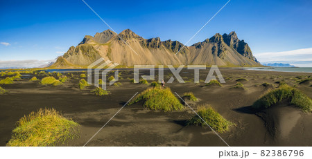 Woman on black sand dune on the Stokksnes headland on southeastern Icelandic coast with Vestrahorn summer panorama of Iceland, Europe. Aerial panoramic shot Woman on black sand dune on the Stokksnes headland on southeastern Icelandic coast with Vestrahorn summer panorama of Iceland, Europe. Aerial panoramic shot 82386796