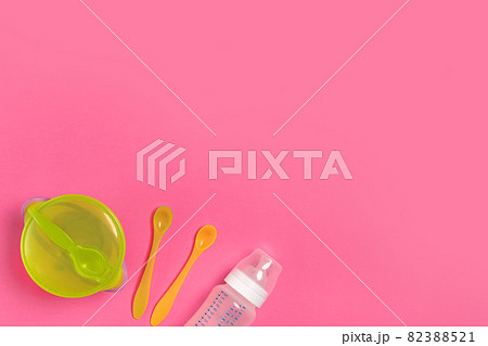 Green plate, a bottle, knife and spoon on pink table. Children dinner time. Top view 82388521