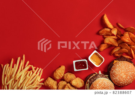 Fast food dish top view. Meat burger, potato chips and nuggets on red background. Takeaway composition. Fast food dish top view. Meat burger, potato chips and nuggets on red background. Takeaway composition. 82388607